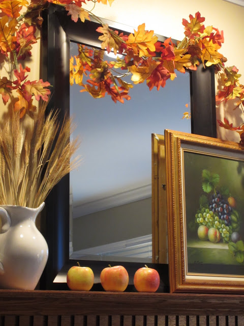 black mirror with leaf garland, apples, artwork and white pitcher with wheat - autumn on the mantel