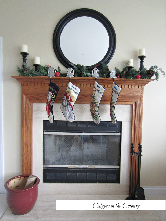 Wood fireplace mantel decorated for Christmas with stockings and round mirror above