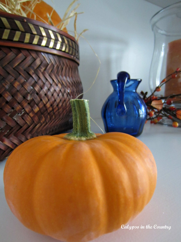 Mini orange pumpkin next to basket and blue glass