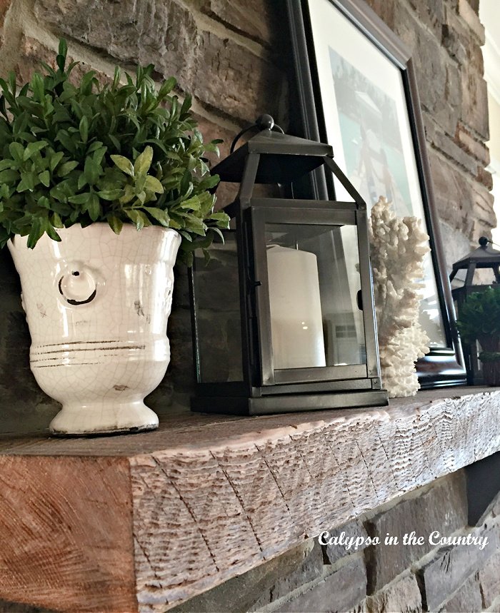 Stone fireplace with rustic wood mantel decorated with plant and lanterns