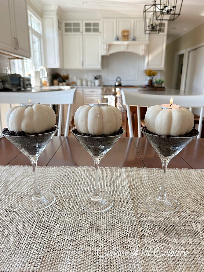 Three pumpkin candles with coffee beans in martini glasses on table - decorating with white pumpkins