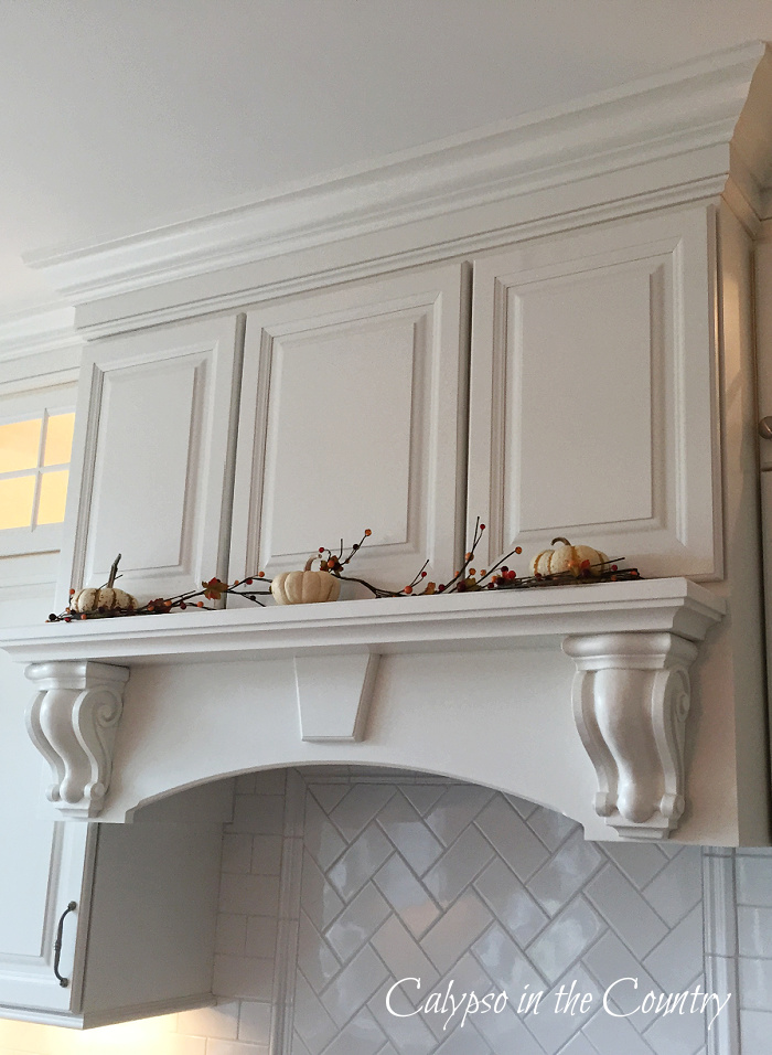 White pumpkins and bittersweet berries on white stove mantel