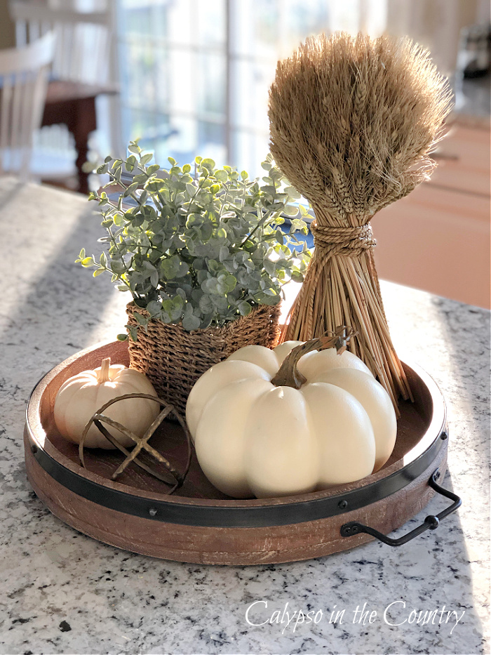 White pumpkins, eucalyptus and wheat stalk on round wooden tray - decorating with white pumpkins