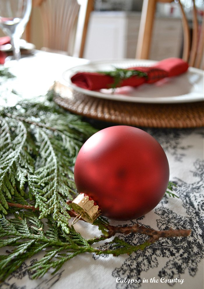 red glass ornament on toile table cloth with greenery