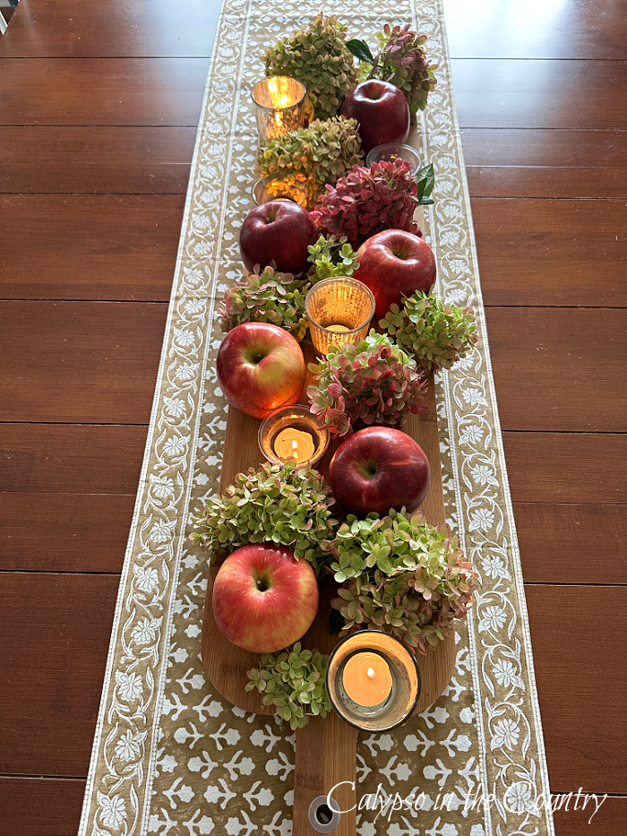 Table centerpiece with apples, hydrangeas and candles on a bread board - decorating with apples