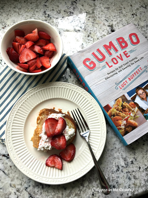 Strawberry poundcake on plate with bowl of strawberries and Gumbo Love Cookbook