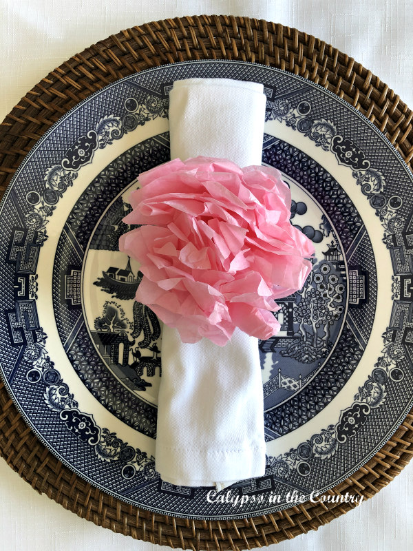 Pink DIY tissue paper flower napkin ring on blue and white plate