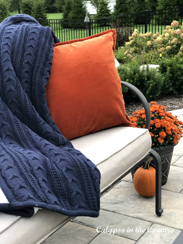 Navy blanket and orange pillow on outdoor sofa - cozy fall patio decorating ideas