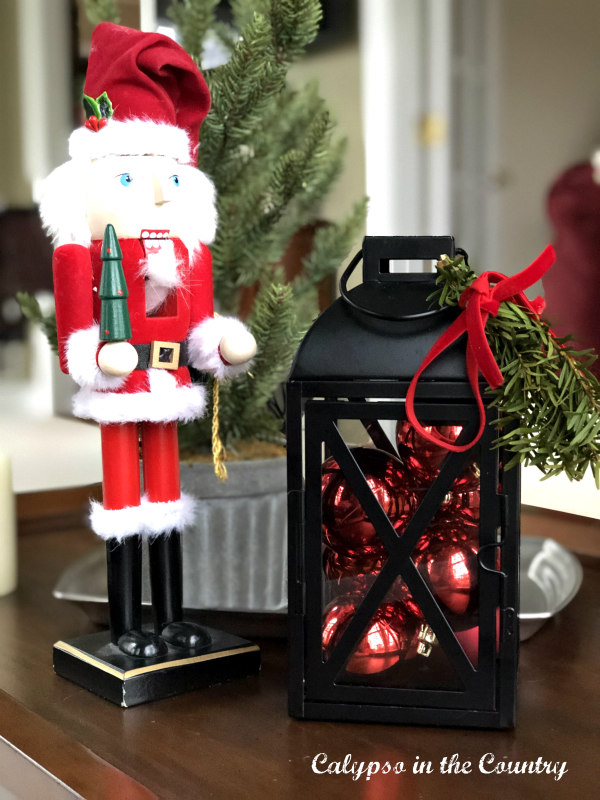 Santa nutcracker and black lantern filled with red ornaments