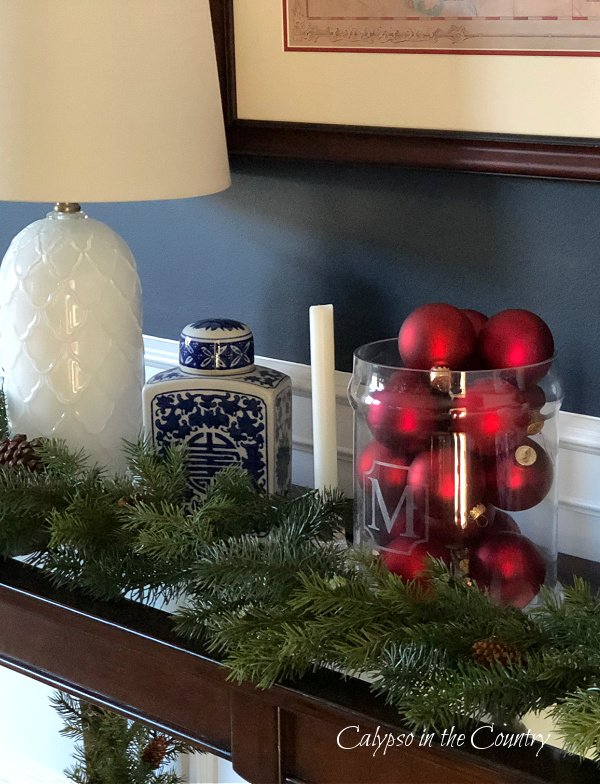 red ornaments in glass container on table with Christmas greenery - easy vase filler ideas