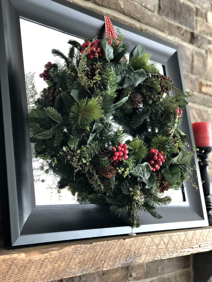 wreath hung on black mirror on fireplace mantel 
