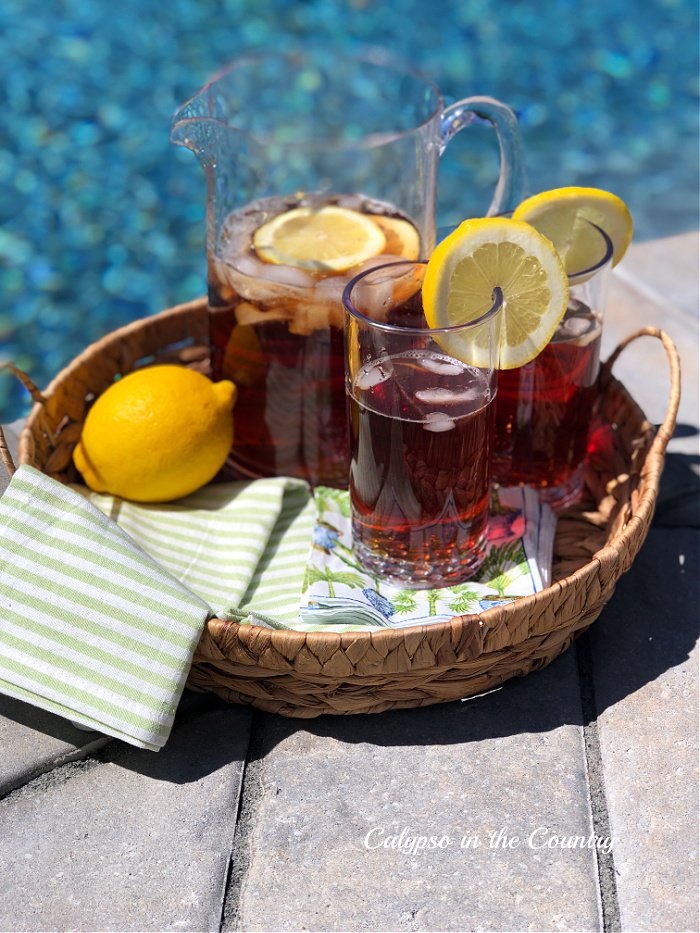 Round seagrass serving tray of iced tea by the pool