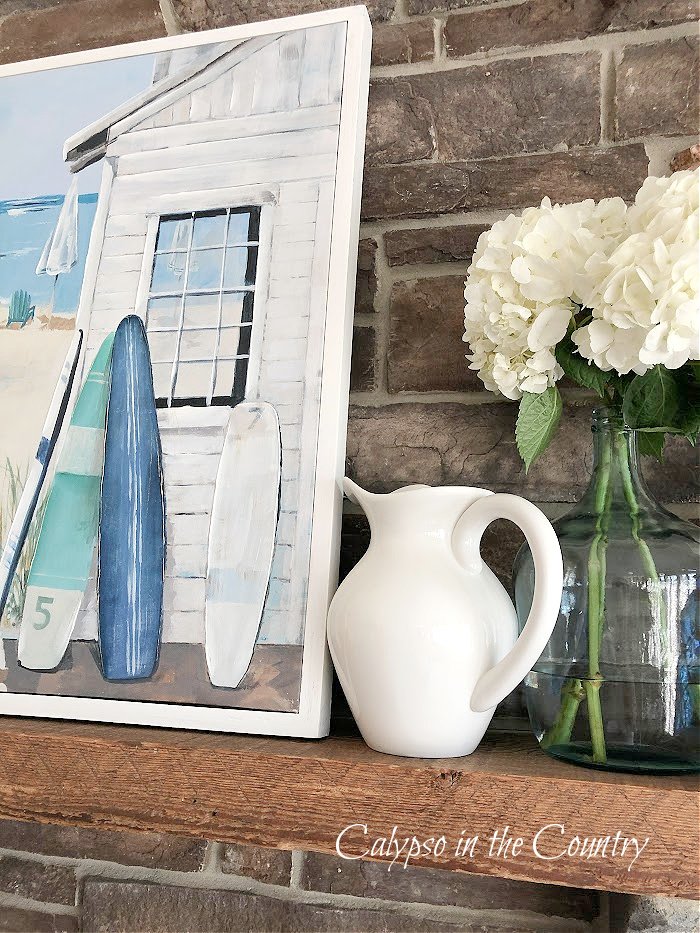 Coastal artwork and white pitcher on stone fireplace - summer decorating ideas