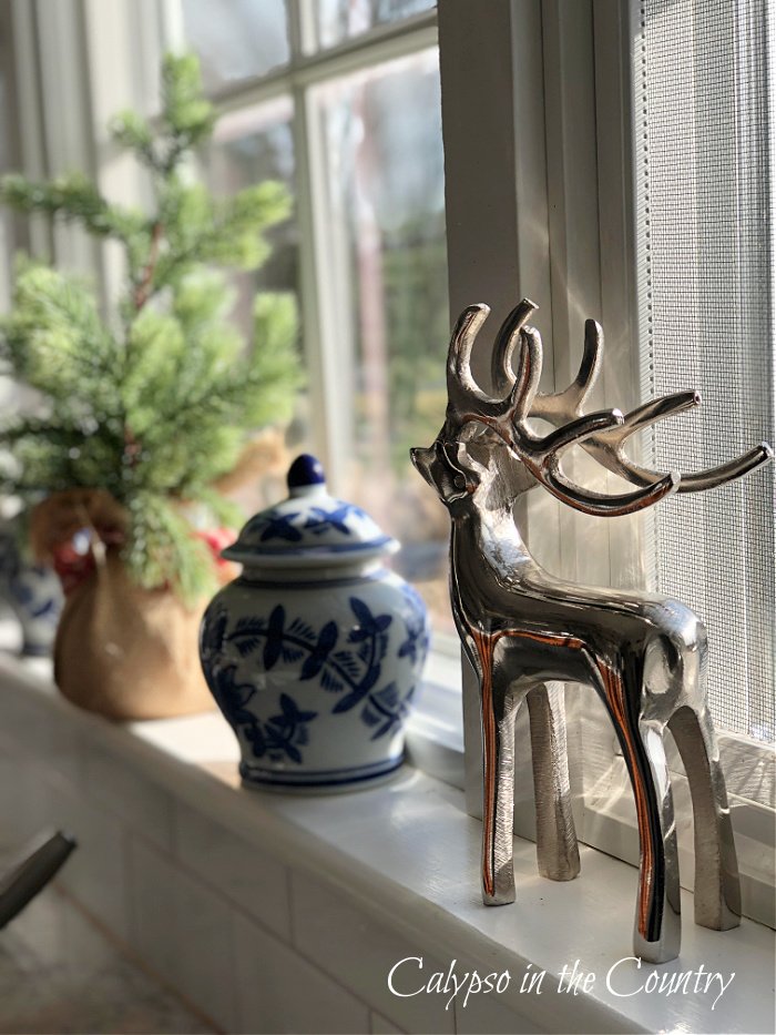 Silver reindeer, little tree and blue and white ginger jar on kitchen window sill - seasonal decorating ideas