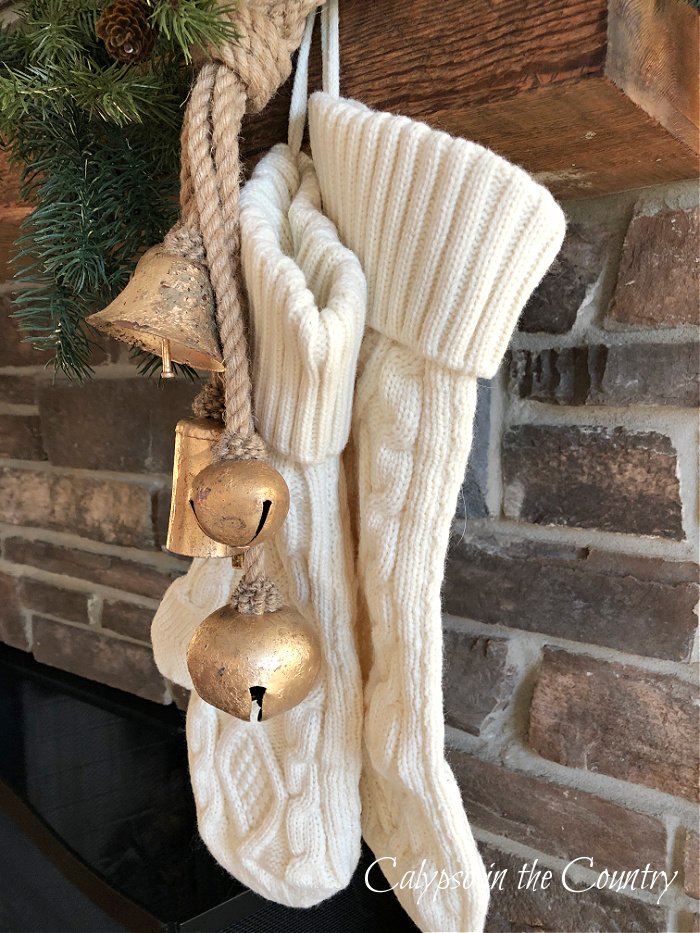 Knit Christmas stockings with gold bells hanging on rustic stone fireplace