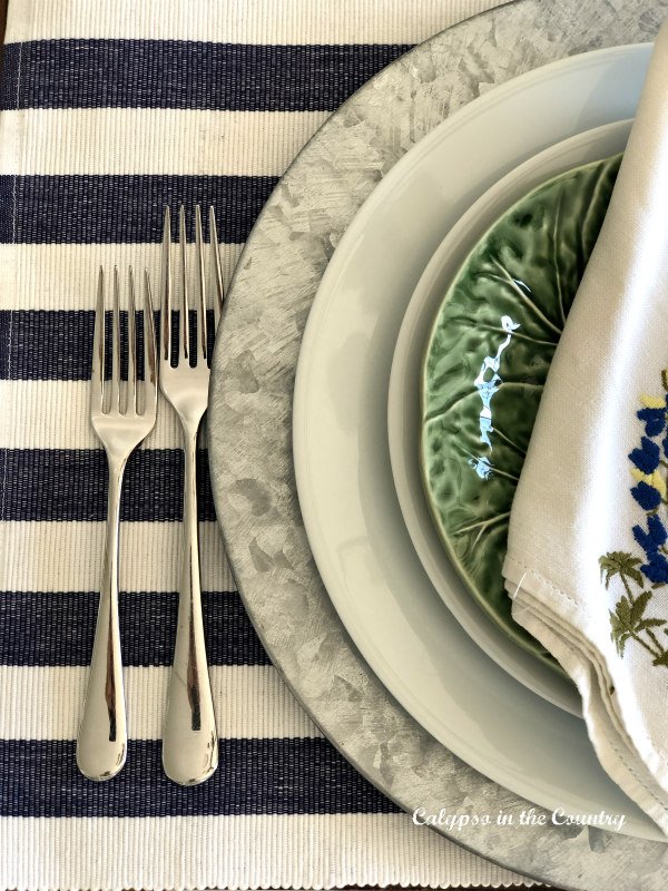 Table place setting with blue and white striped placemat and cabbage plates over white plates.
