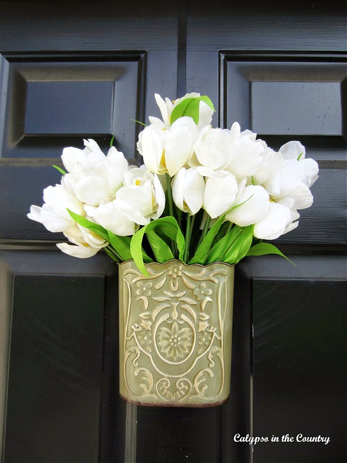 White tulips in metal container hanging on black door - spring door decor