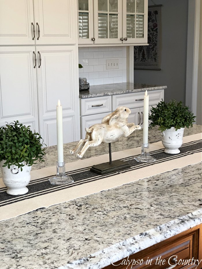 Bunny statue and greenery displayed on table runner on kitchen island - kitchen island decorating ideas