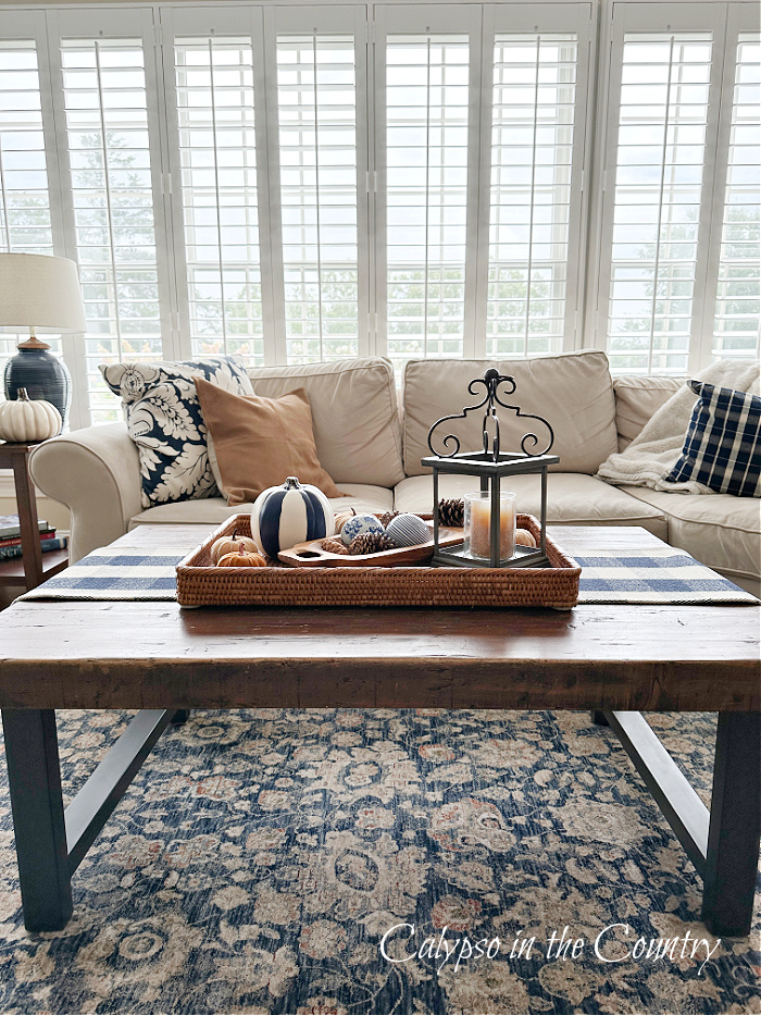 Coffee table with rattan tray in front of sectional and plantation shutters - fall decorating 