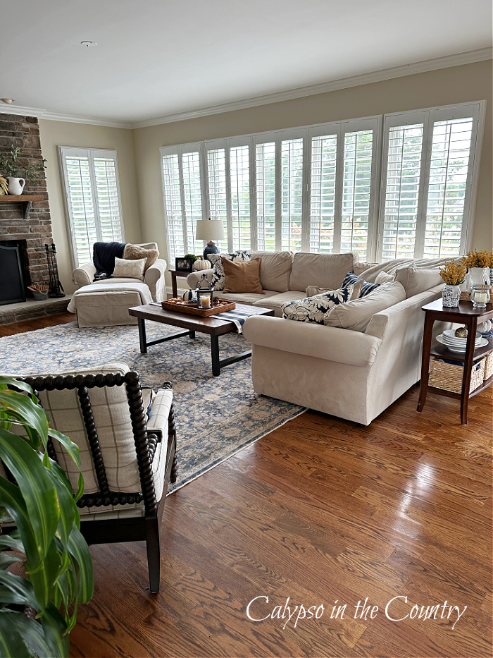 Family room with plantation shutters, sectional sofa, wood floors and blue rug - fall aesthetic ideas.