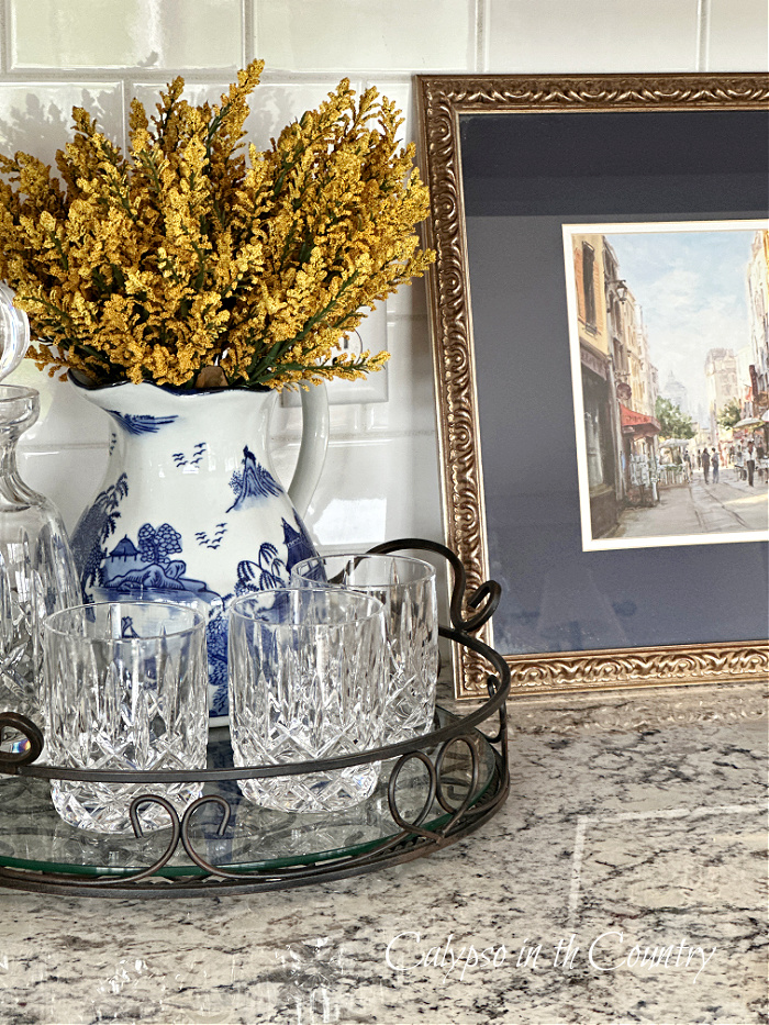 Blue and white pitcher with yellow stems on tray next to navy blue artwork - fall aesthetic ideas 