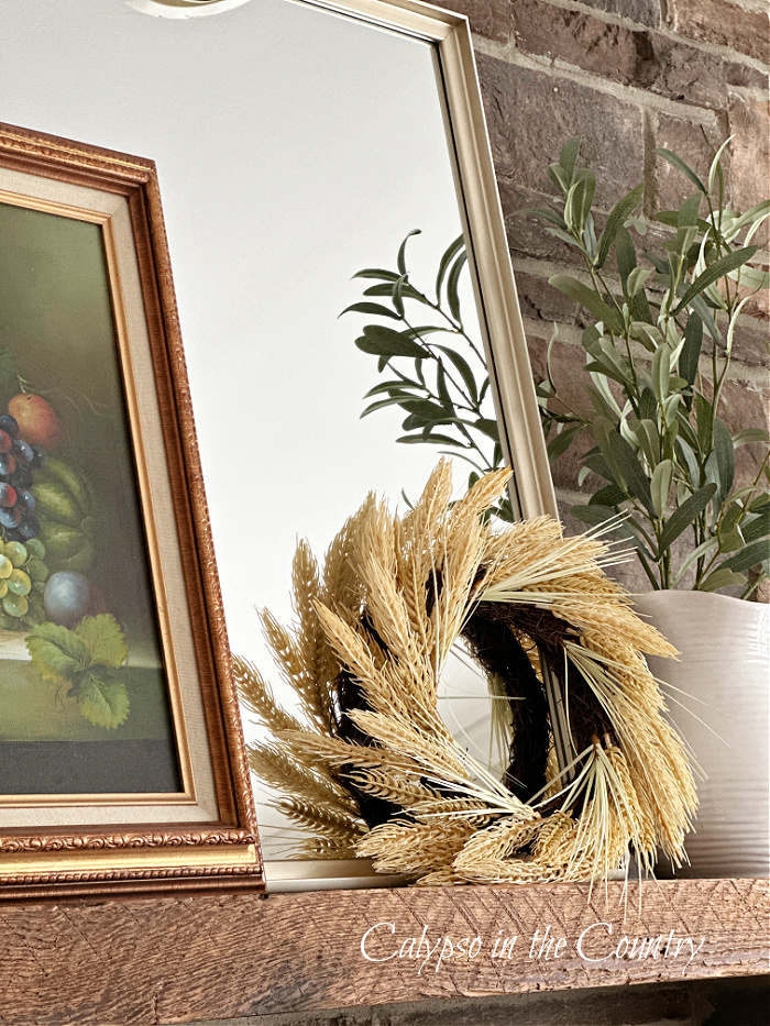 Mirror, artwork and wheat wreath leaning on rustic wood mantel - fall home decor