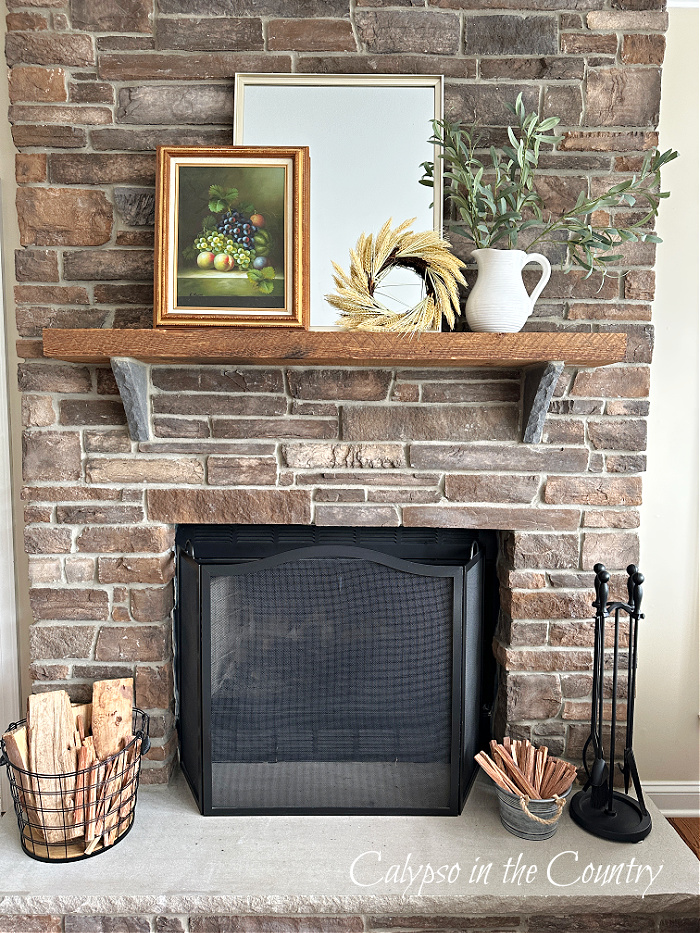 Stone fireplace with artwork, greenery and mirror on rustic wood mantel - fall aesthetic ideas