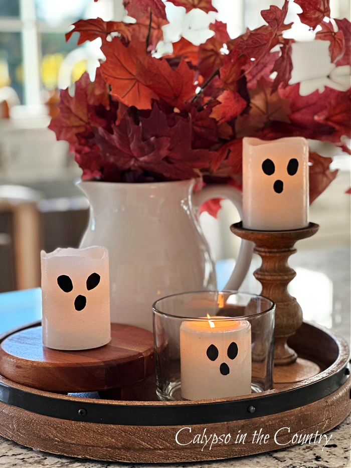 Three ghost candles on wooden tray with white pitcher of red leaves - DIY Halloween ghost decorations