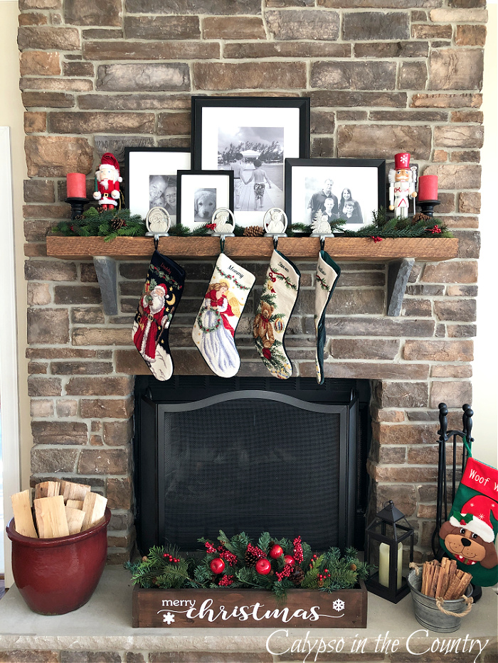 Black and white family photos and four Christmas stockings on wood mantel on stone fireplace