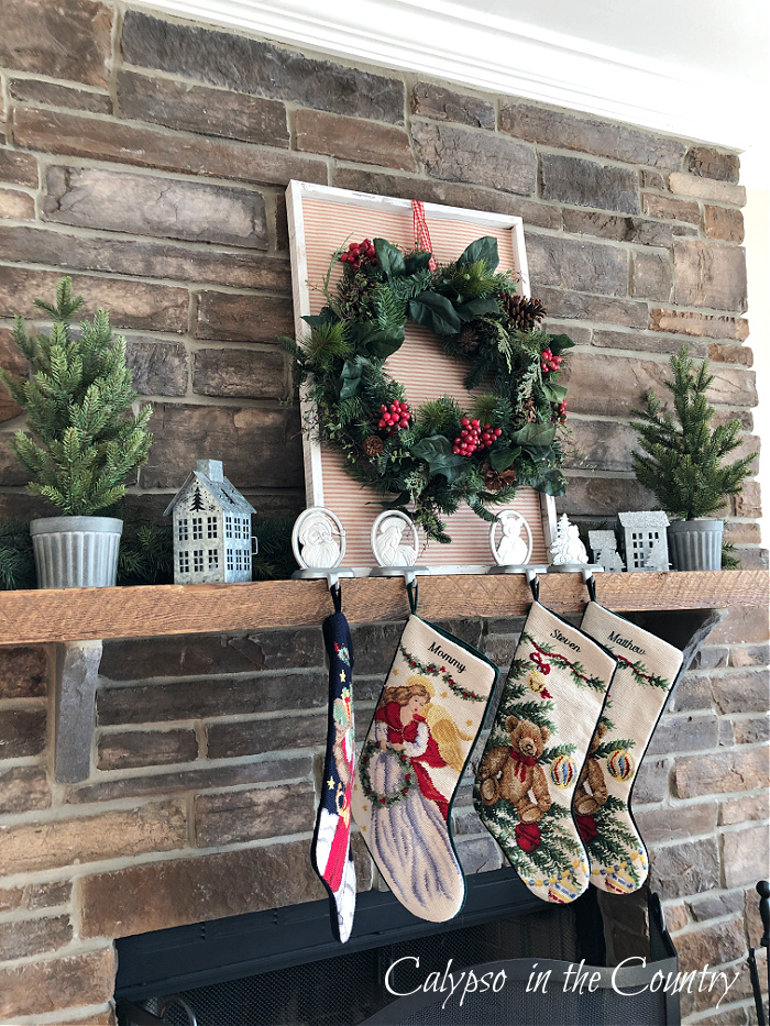 Stone fireplace with leaning wreath and stockings hung on rustic wood mantel