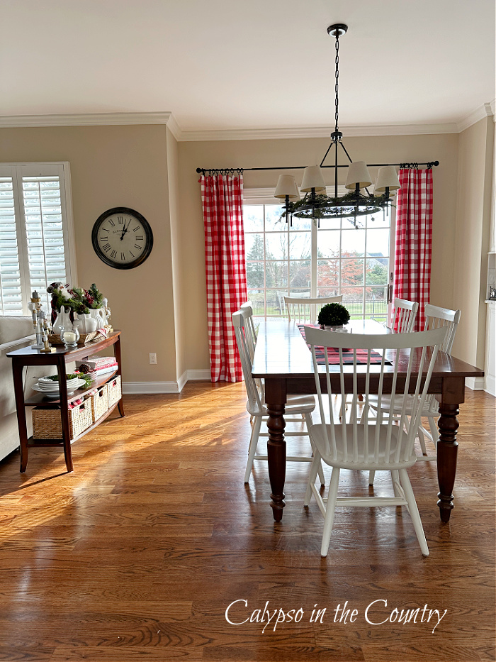 Kitchen table with white chairs in front of doors with red checked curtains - cozy Christmas home tour