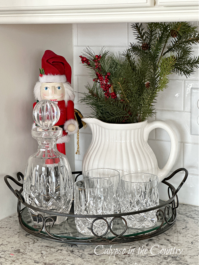 Countertop vignette with tray of glasses, nutcracker and white pitcher of greenery - cozy Christmas home tour
