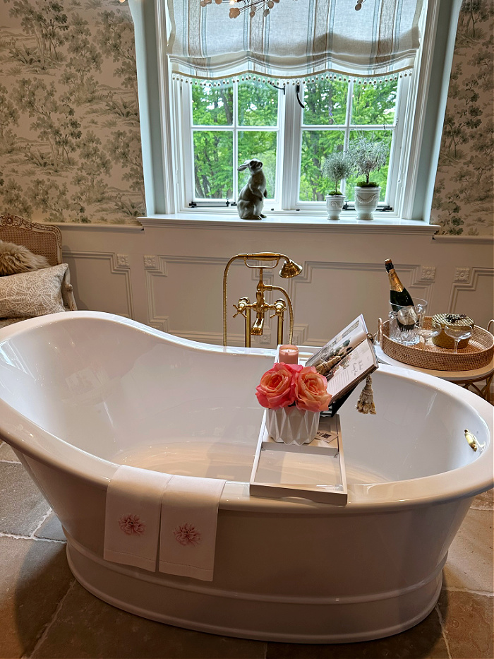 Freestanding tub in front of window in toile wallpapered bathroom