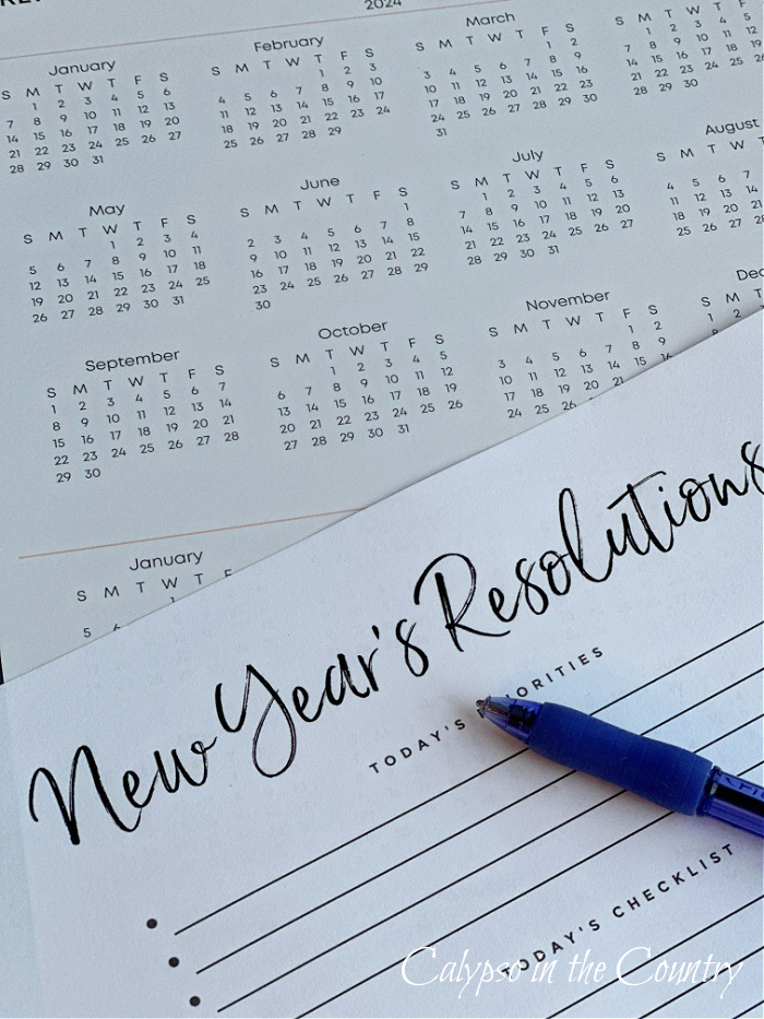 Calendar and blank list of New Year's resolutions with blue pen.