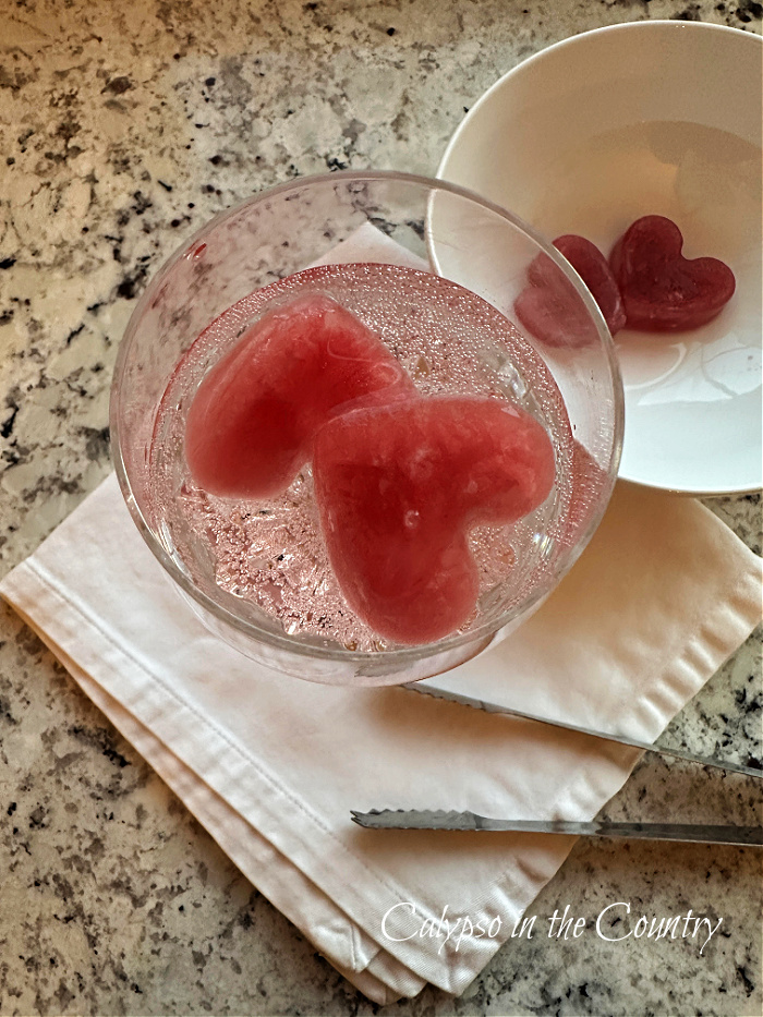 red heart shaped ice cubes in glass of seltzer