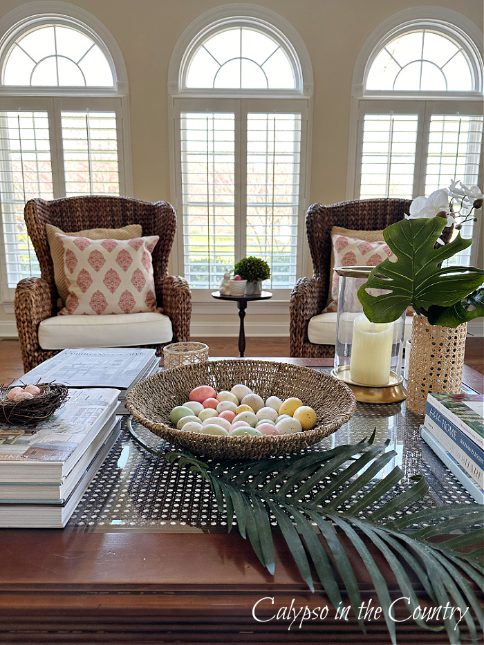 Wood coffee table decorated with woven bowl full of eggs, palm leaves and stacks of books - Easter Vignettes