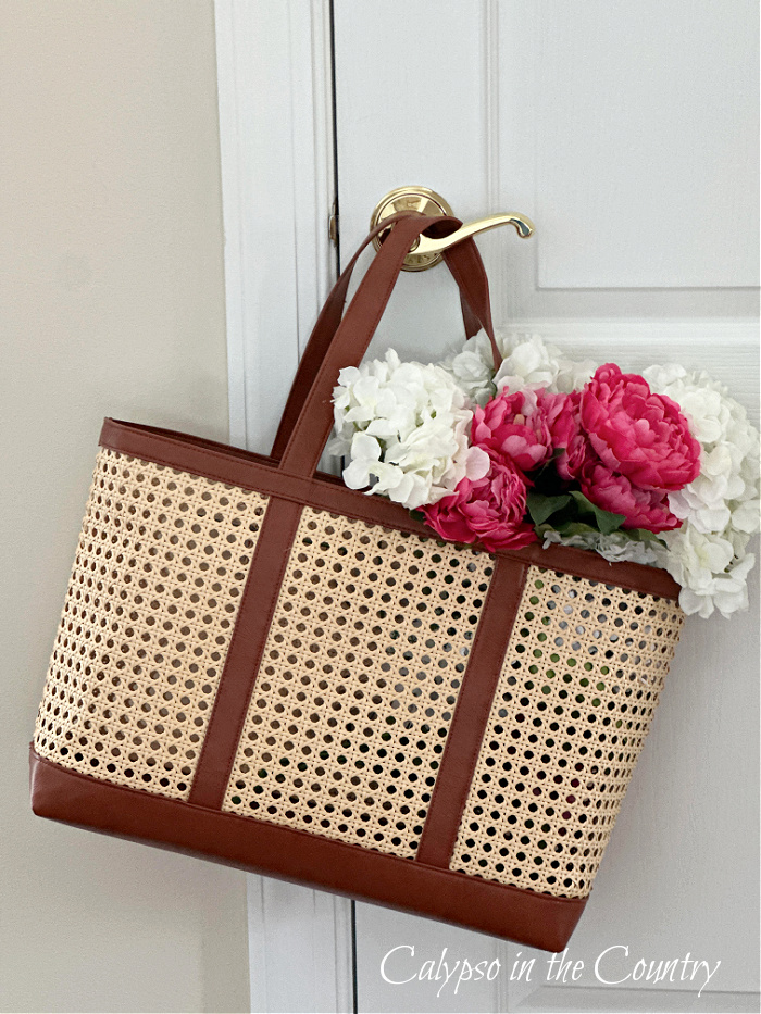 Cane tote bag filled with flowers and hanging on door knob - welcome april