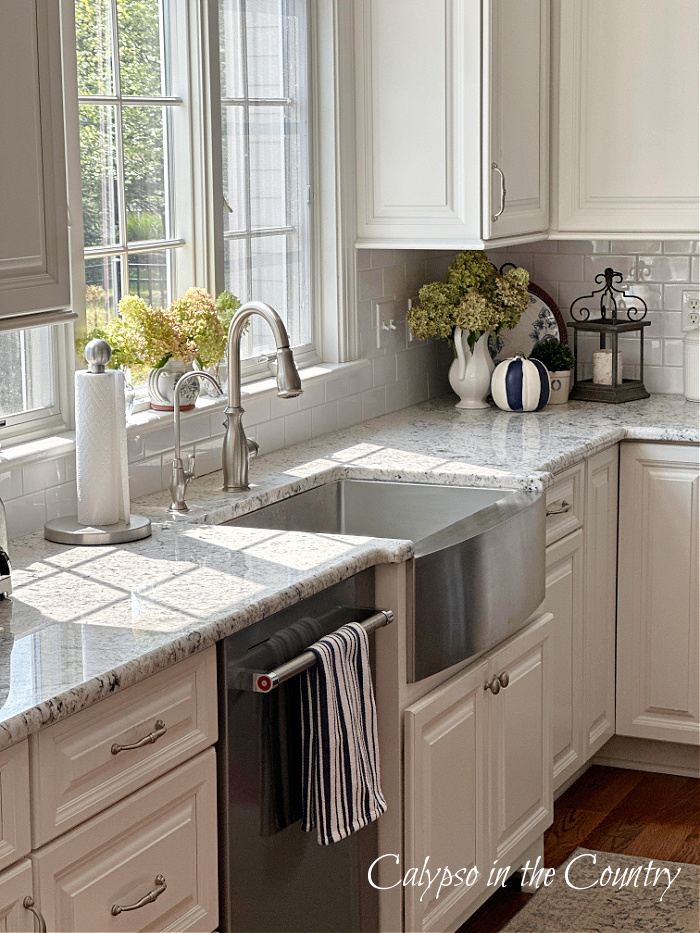 Hydrangeas in windows over kitchen sink with white cabinets 