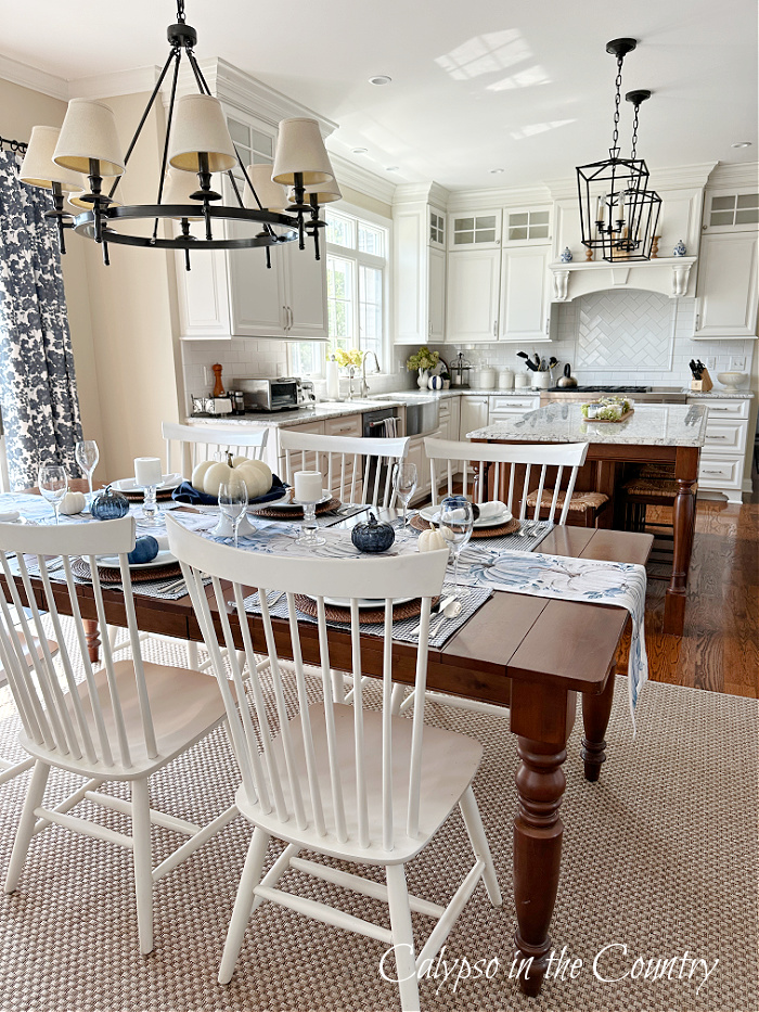 White kitchen with brown wood table and white chairs decorated with blue and white for fall