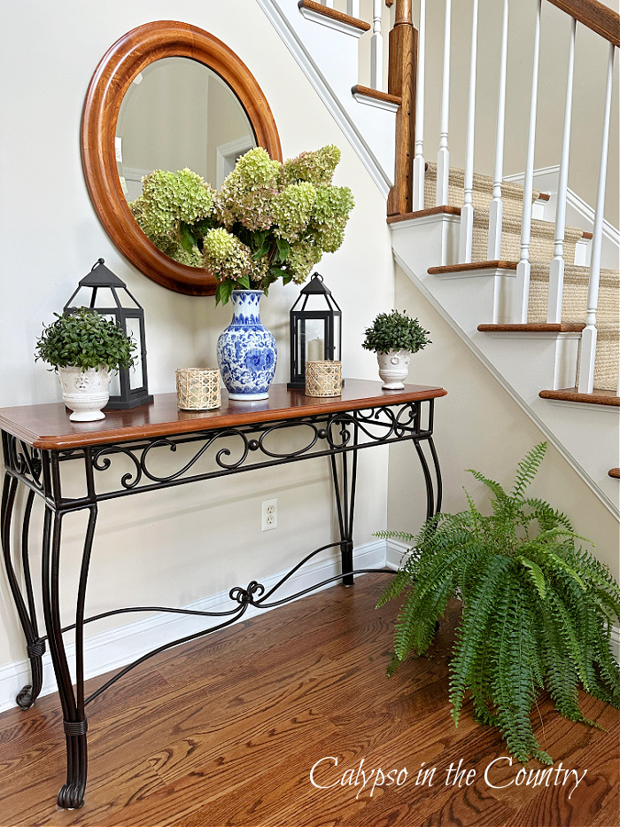 Staircase with foyer table decorated for fall with blue and white vase filled with green hydrangeas
