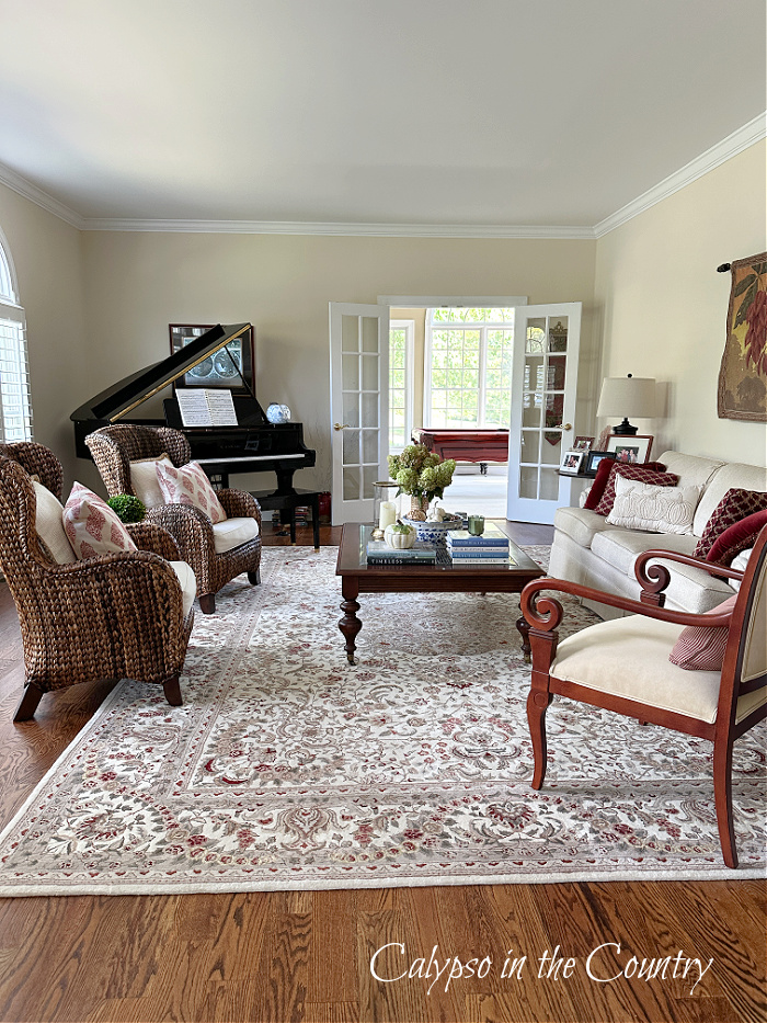 Living room with oriental rug, seagrass chairs, black piano and coffee table decorated with blue and white fall items