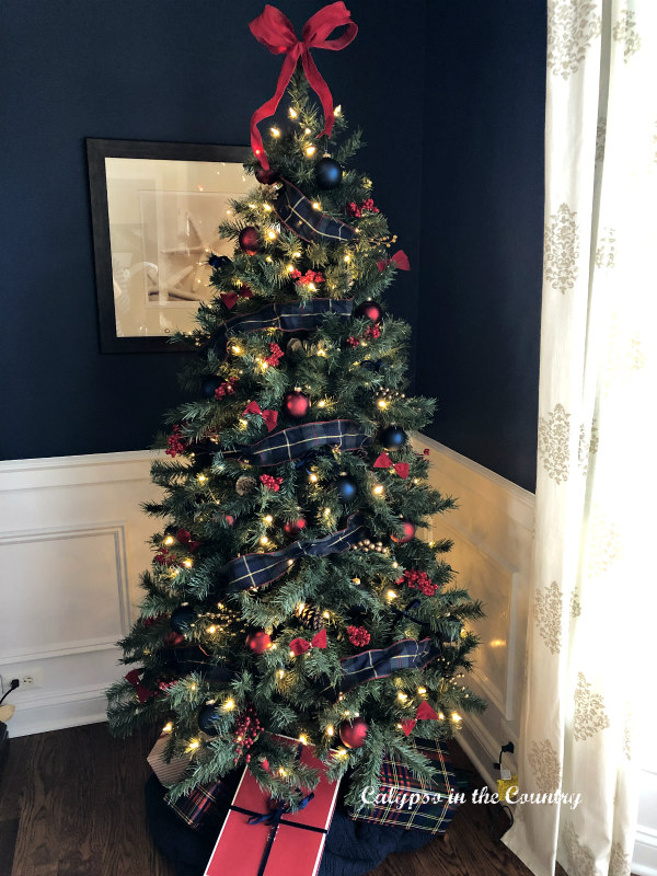 Christmas tree in corner of navy dining room decorated with plaid ribbon