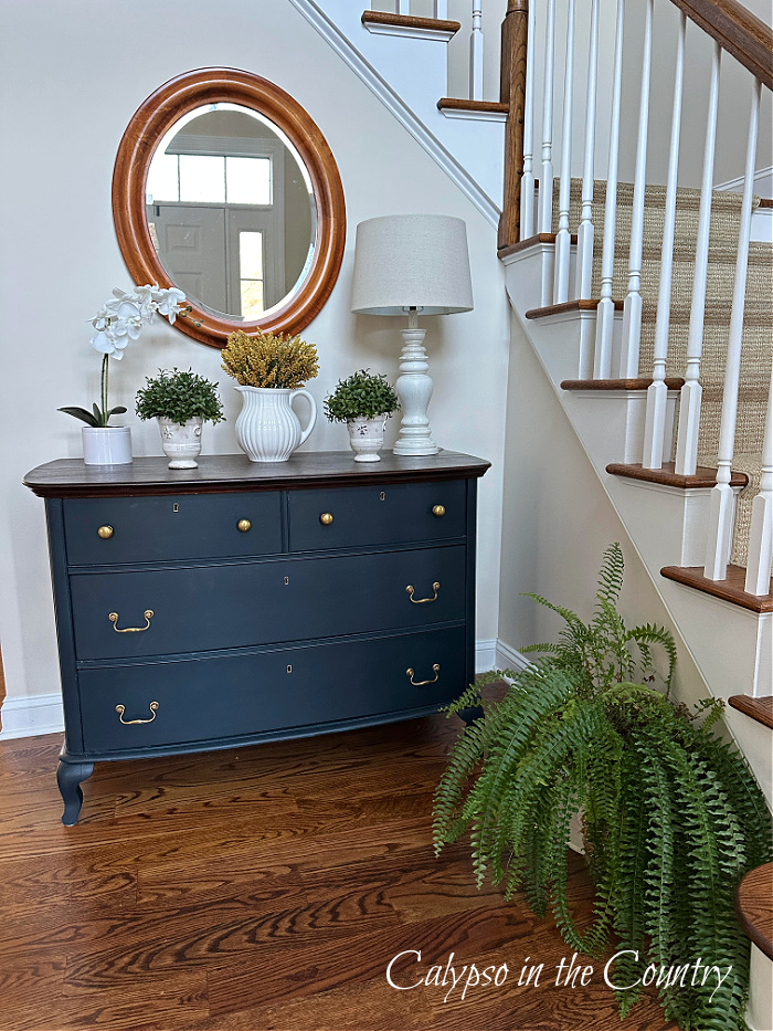 Blue dresser next to staircase in foyer with wood floors
