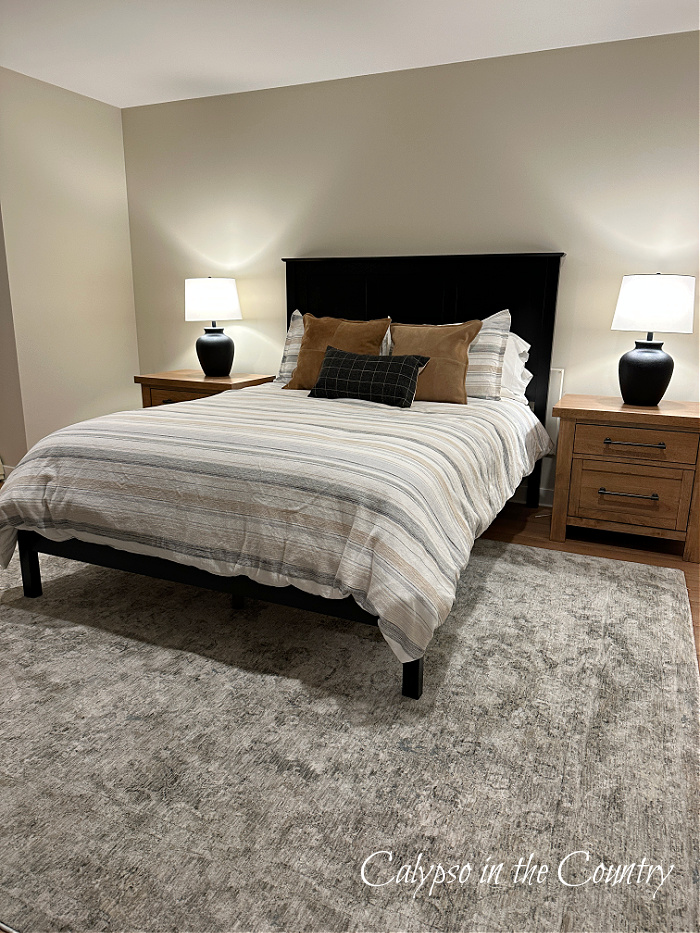 Tan bedroom with black bed with tan and gray striped bedding and black lamps on wood nightstands - neutral bedroom makeover