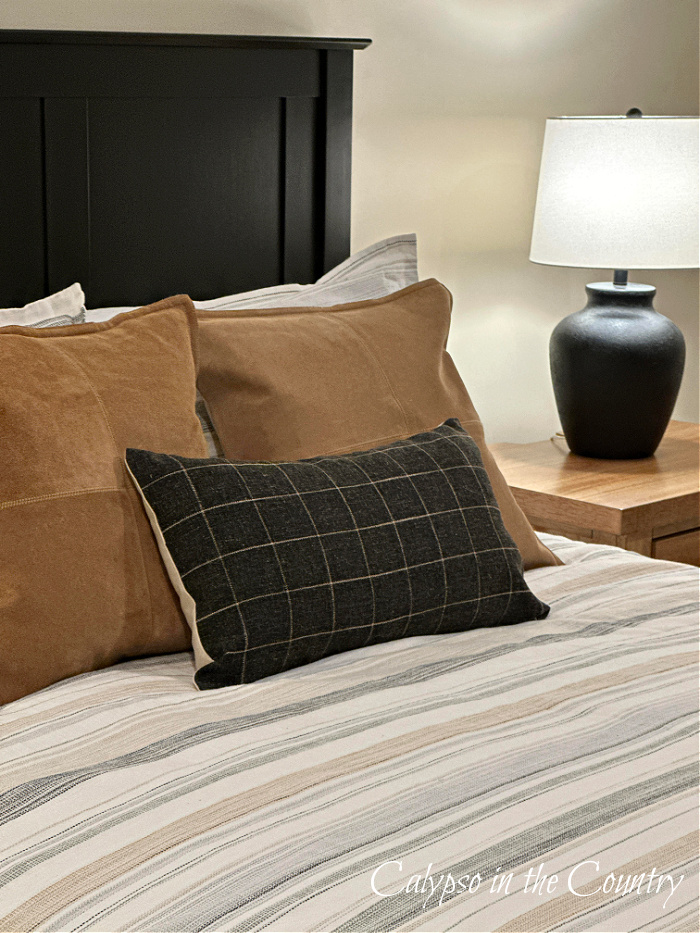black headboard with tan throw pillows and black plaid throw pillow on neutral striped comforter 