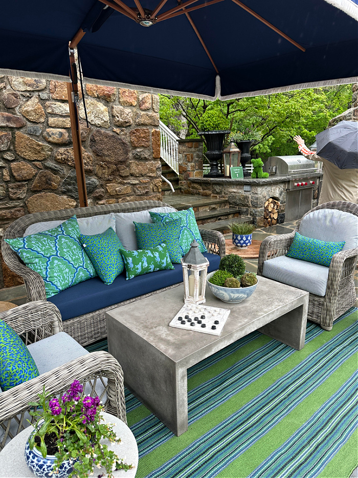Blue and green fabrics on outdoor furniture under navy blue umbrella for patio season