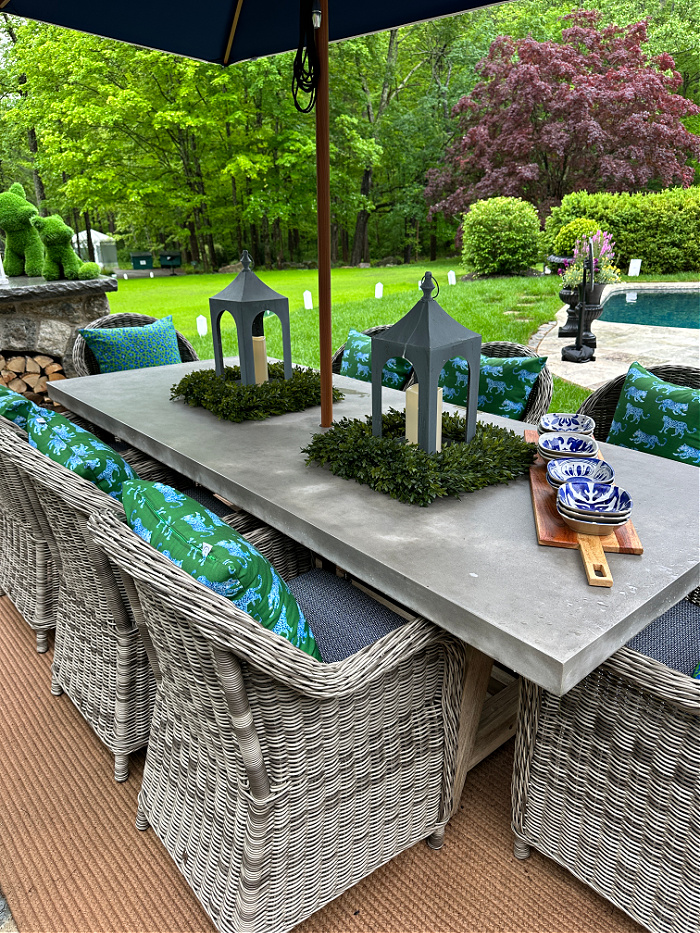 Stone rectangular table with gray wicker chairs and blue and green pillows on patio by pool