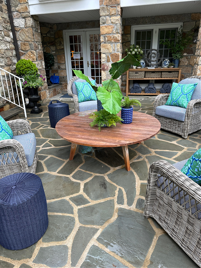Outdoor wicker chairs with blue and green pillows surrounding wood coffee table on stone patio