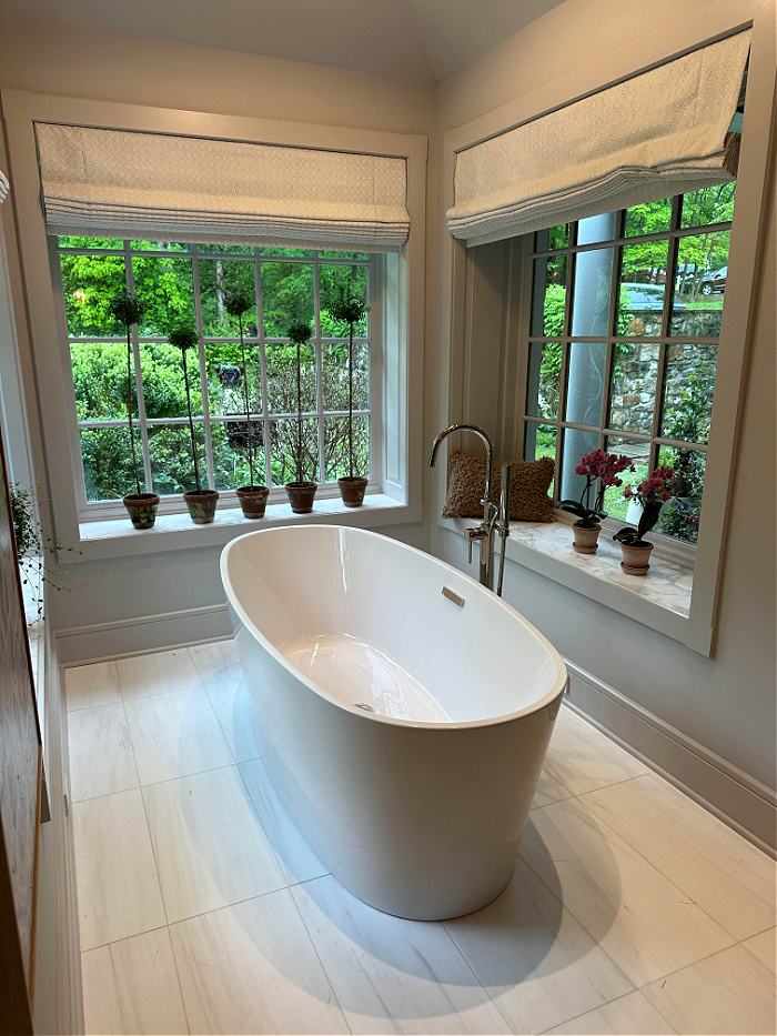 Freestanding white bathtub surrounded by large windows with tall topiaries on the window sills - May recap