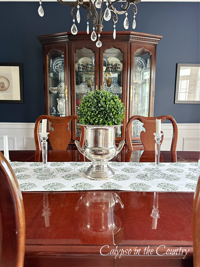 Navy dining room with cherry hutch and table decorated with boxwood sphere in silver urn - june recap